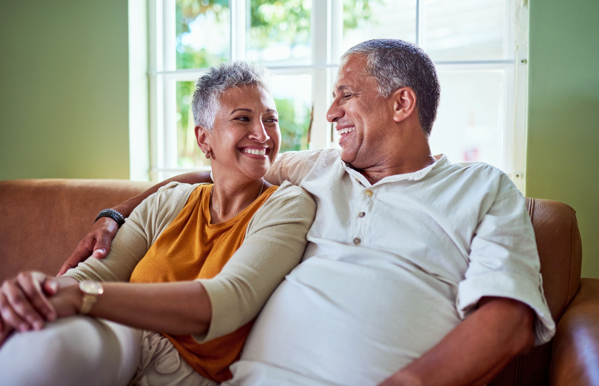 Happy, love and smile senior couple hug relax and sitting on a couch at home. Elderly man and woman smiling and enjoying quality bonding together in the living room sofa and having fun in the house