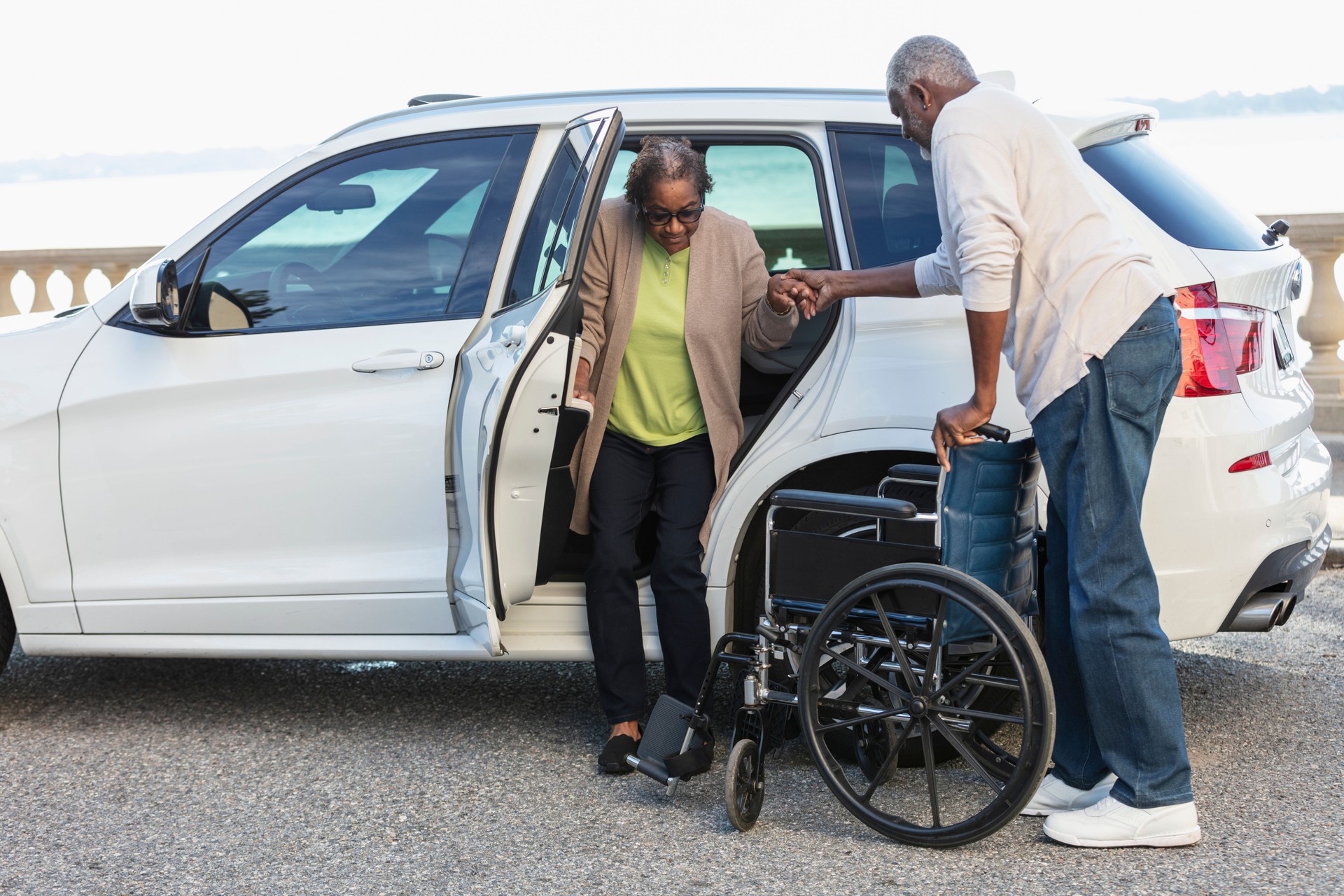 Senior woman exiting car into wheelchair, spouse helping